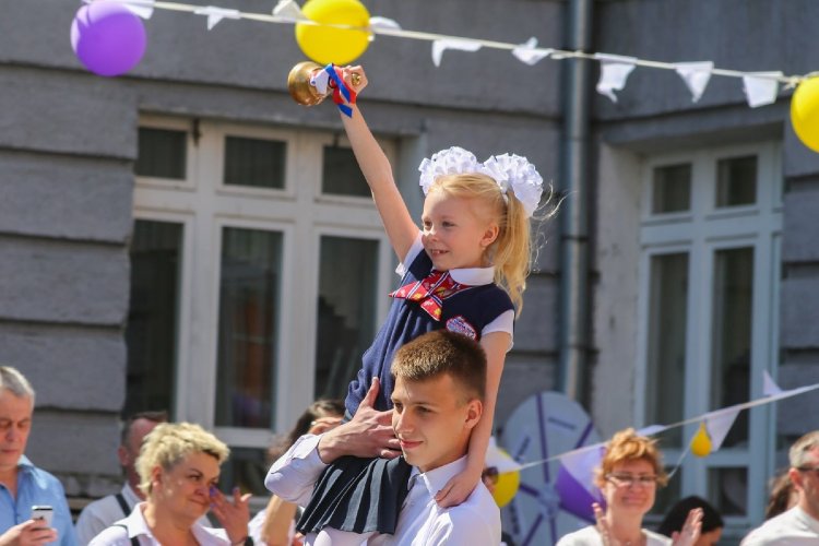 Первоклассницв, усаженная на плечи 11-классника, звонит в школьный колокольчик